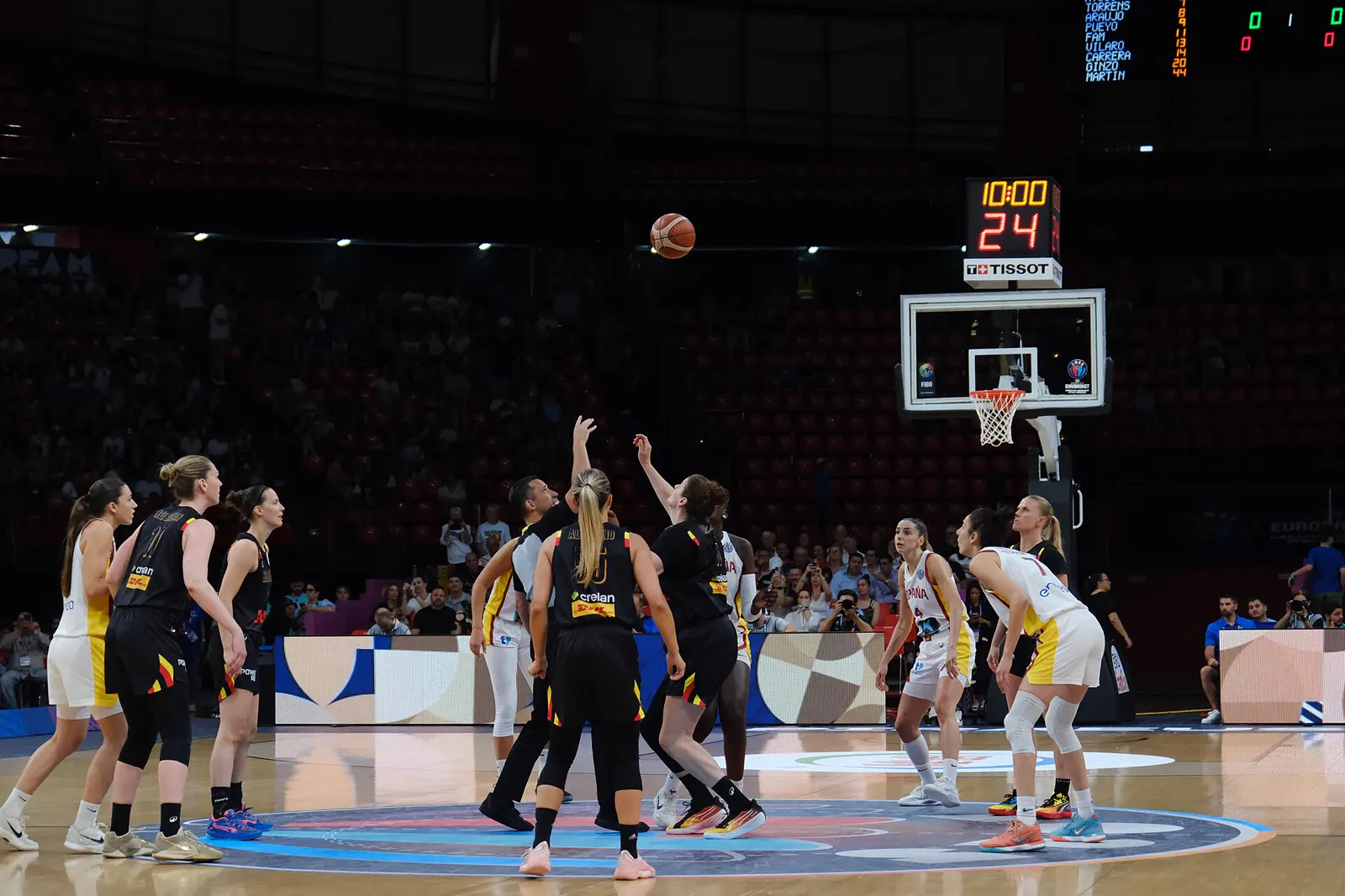 Salto inicial de un partido de baloncesto entre jugadoras de España, de blanco, y de Bélgica, de negro, con el marcador a cero