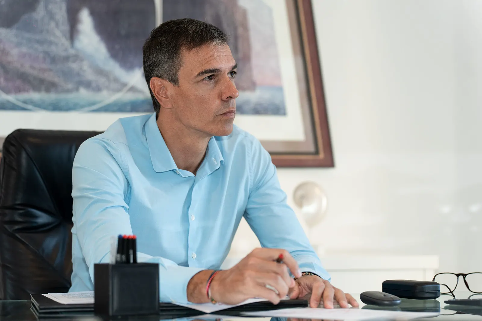 Pedro Sánchez, sentado ante una mesa de despacho con papeles y un bolígrafo en la mano, escucha con la mirada fija fuera de plano