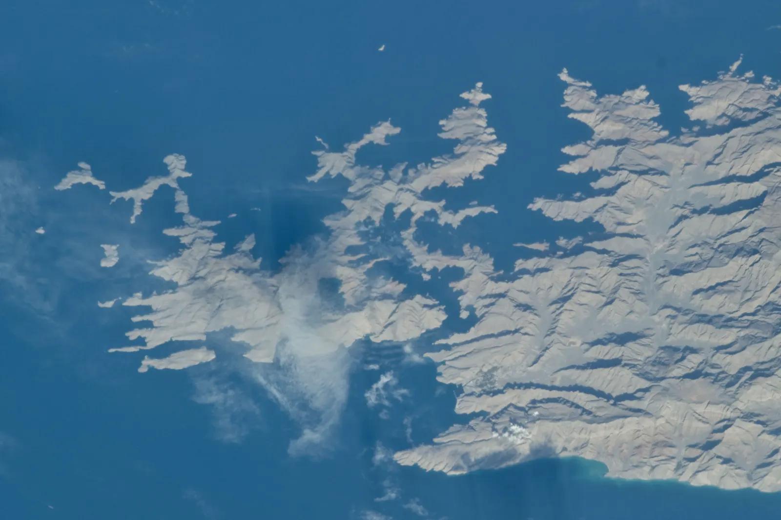 Vista desde el espacio de una península montañosa y árida, recortada por decenas de entrantes de mar, que se adentra en un océano azul intenso.