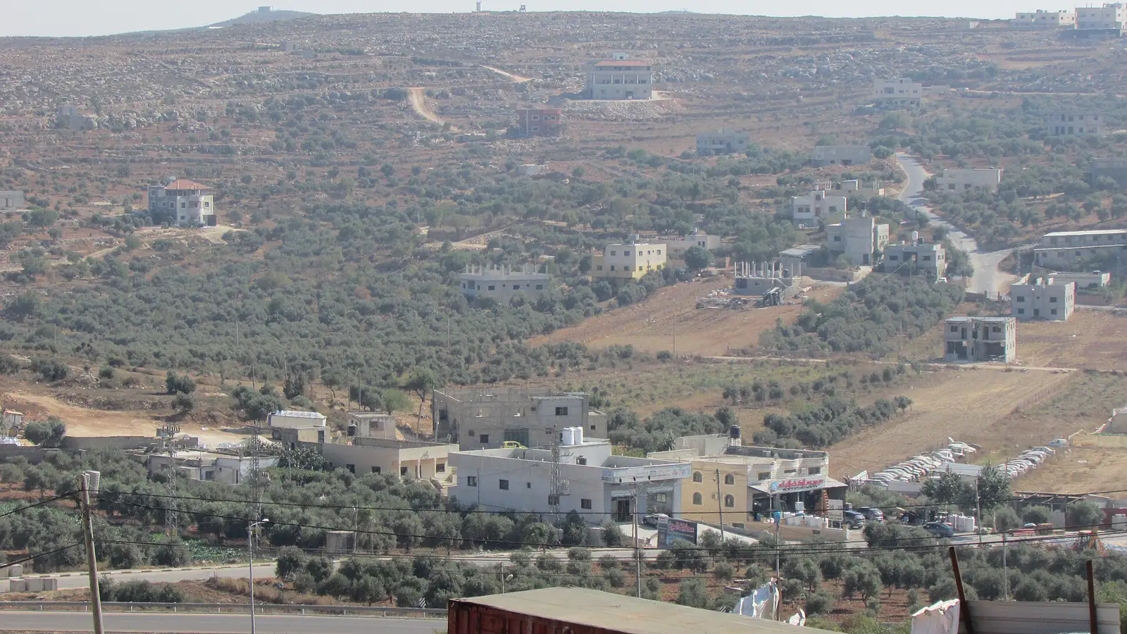 Vista general de la localidad palestina de Qusra: casas de bloque y piedra dispersas entre olivares, con una ladera pedregosa al fondo.