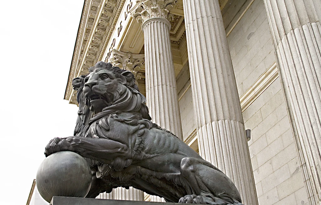 Detalle de la fachada principal del Congreso de los Diputados en Madrid: columnas clásicas y frontón de piedra, con uno de los leones de bronce en primer término sobre su pedestal.