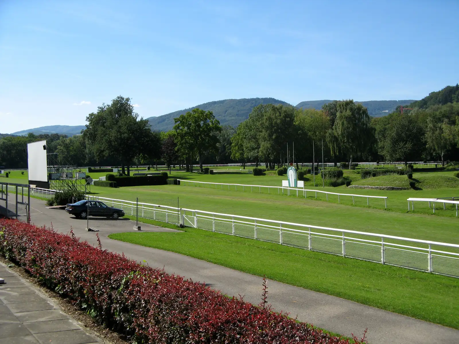 Pista de hierba del hipódromo del Schachen, en Aarau, con vallas blancas, arbolado y colinas al fondo