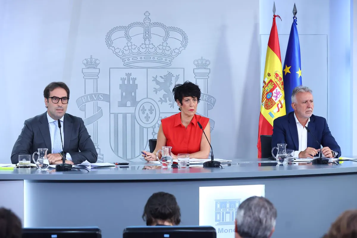 Tres ministros sentados tras una mesa larga con micrófonos en la sala de prensa de La Moncloa, ante el escudo de España y las banderas española y europea.