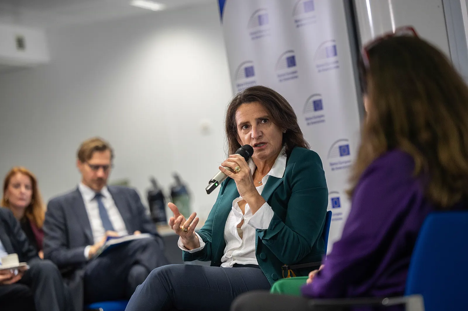Teresa Ribera, sentada y con un micrófono en la mano, interviene en un acto de la Comisión Europea ante otros participantes