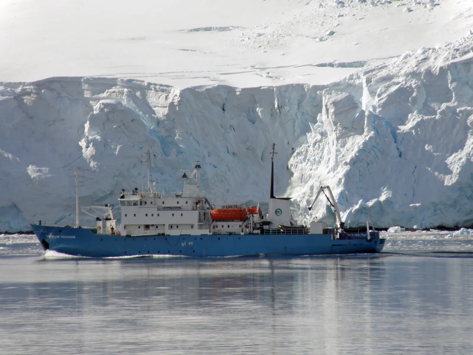 El buque de casco azul "Profesor Molchanov" navega en aguas polares frente al frente de un glaciar cubierto de nieve.