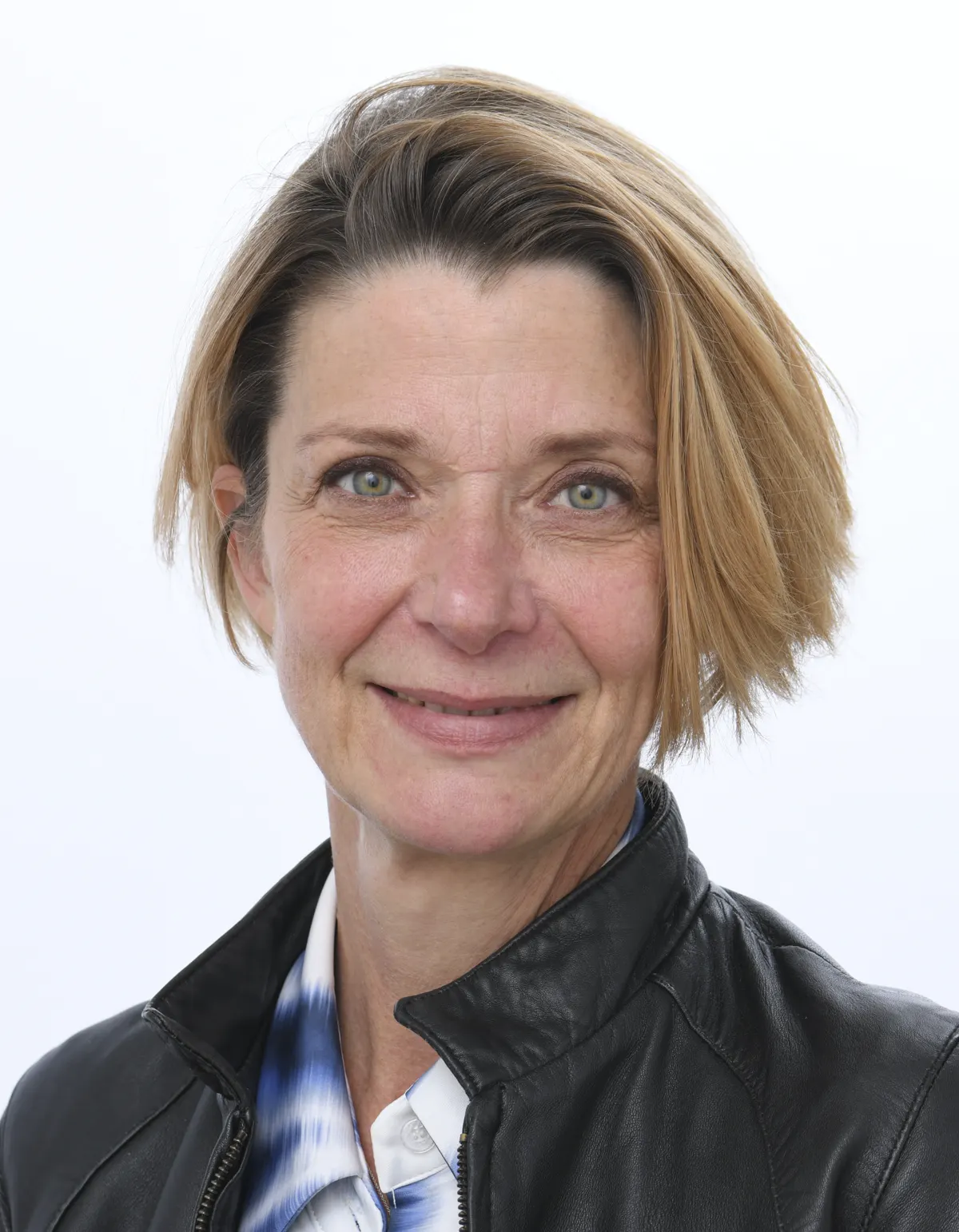 Retrato oficial de la eurodiputada Estelle Ceulemans: mujer de media melena rubia, con cazadora de cuero negra sobre una camisa blanca de estampado azul, sonriendo ante un fondo blanco.