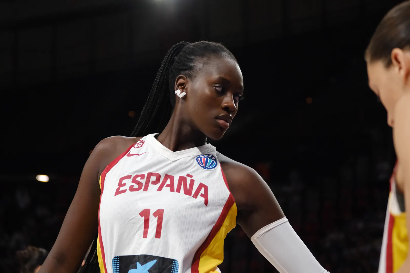 La jugadora Awa Fam, con la camiseta blanca de España y el dorsal 11, mira hacia la pista durante un partido