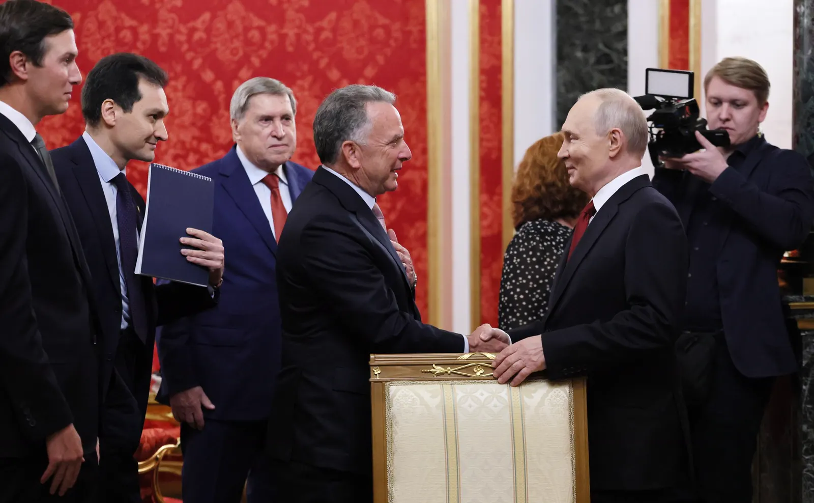 Vladímir Putin estrecha la mano de Steve Witkoff en una sala del Kremlin de paredes rojas; a la izquierda espera Jared Kushner junto a otros dos miembros de las delegaciones, y a la derecha graba un cámara de televisión.