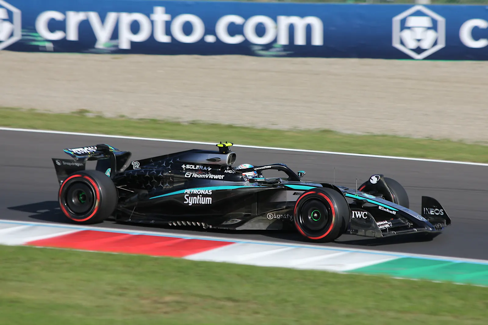 Monoplaza negro de Mercedes con el número 12 rodando sobre el asfalto del circuito de Monza, con los pianos rojos y blancos de una curva y una valla publicitaria al fondo