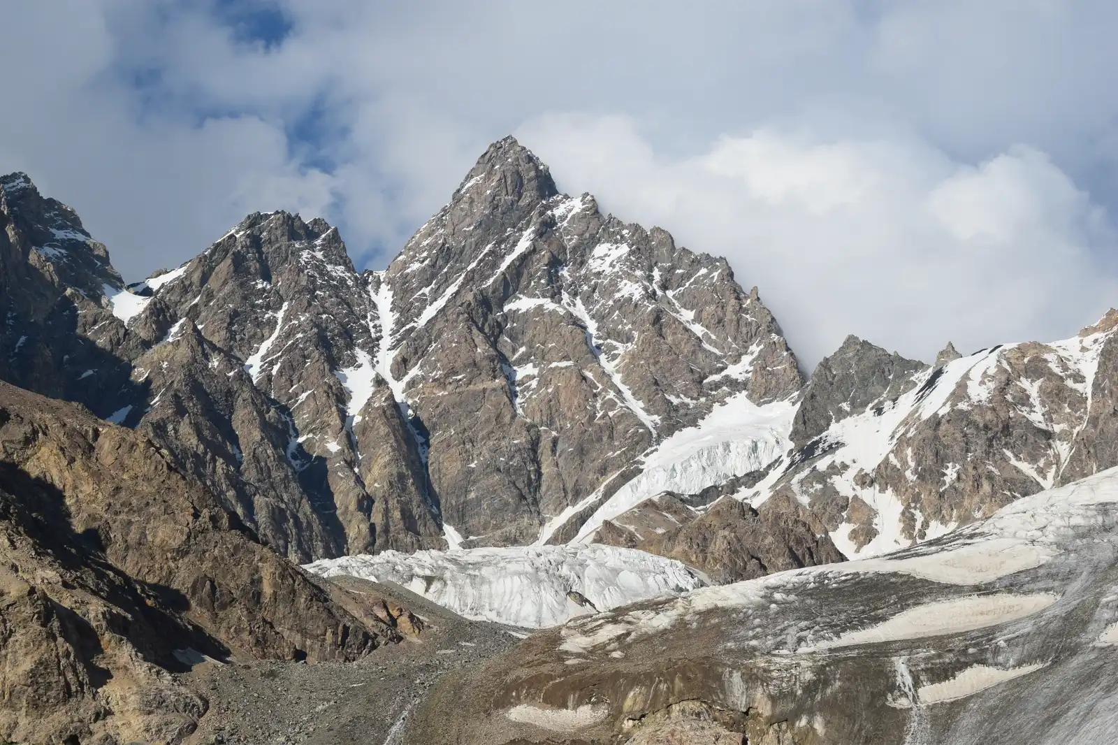 Cumbre rocosa y afilada del monte Mizhirgi, con nieve en los canalones y un glaciar a sus pies, bajo un cielo con nubes bajas.