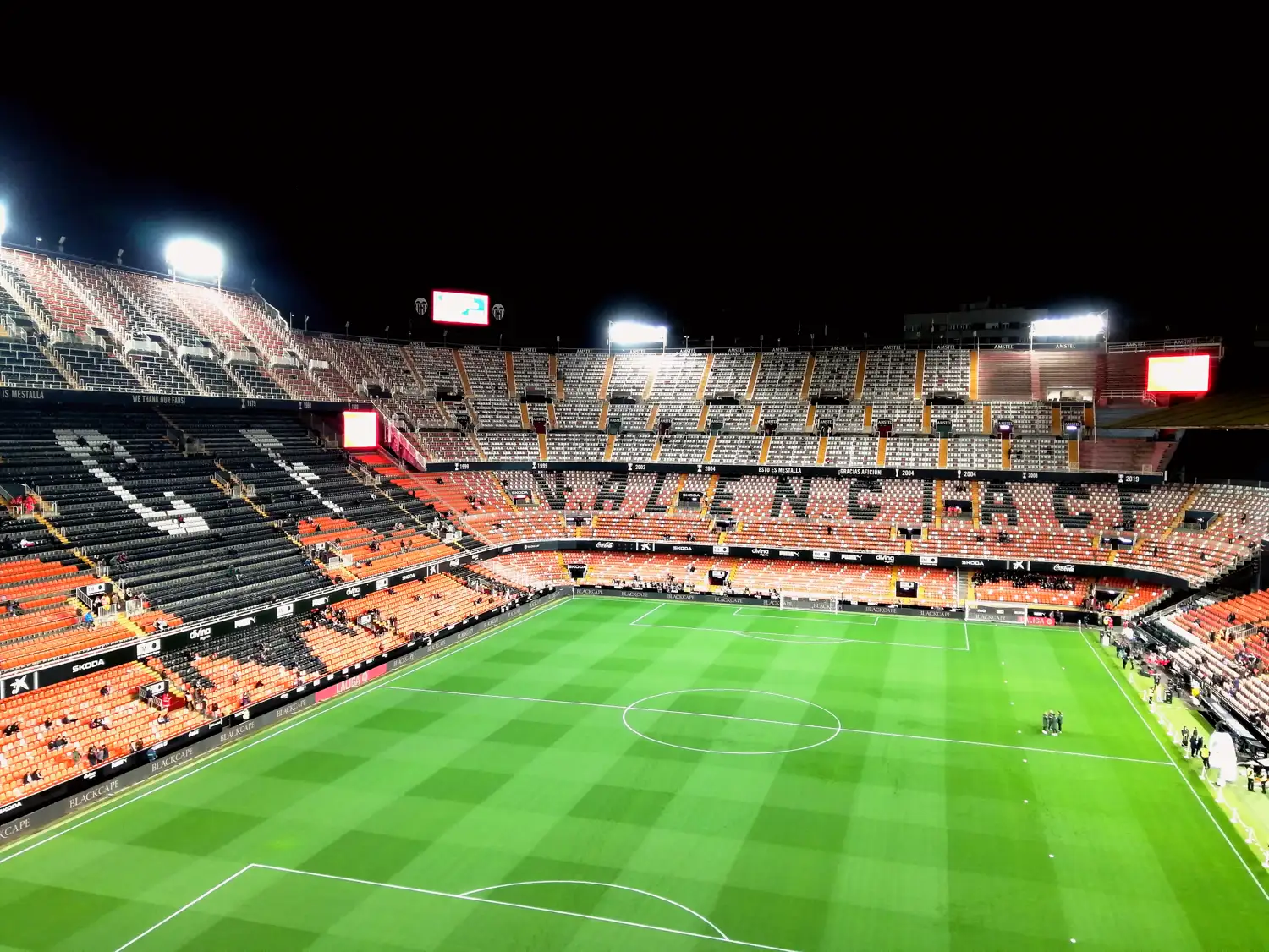 Vista del interior del estadio de Mestalla desde la grada alta, con el césped iluminado y las gradas casi llenas antes del comienzo de un partido.