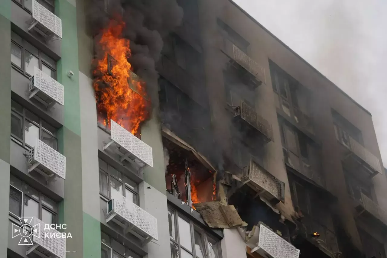 Fachada de un edificio de viviendas de Kiev con dos plantas ardiendo, llamas saliendo por un balcón, humo negro y balcones reventados por la explosión.