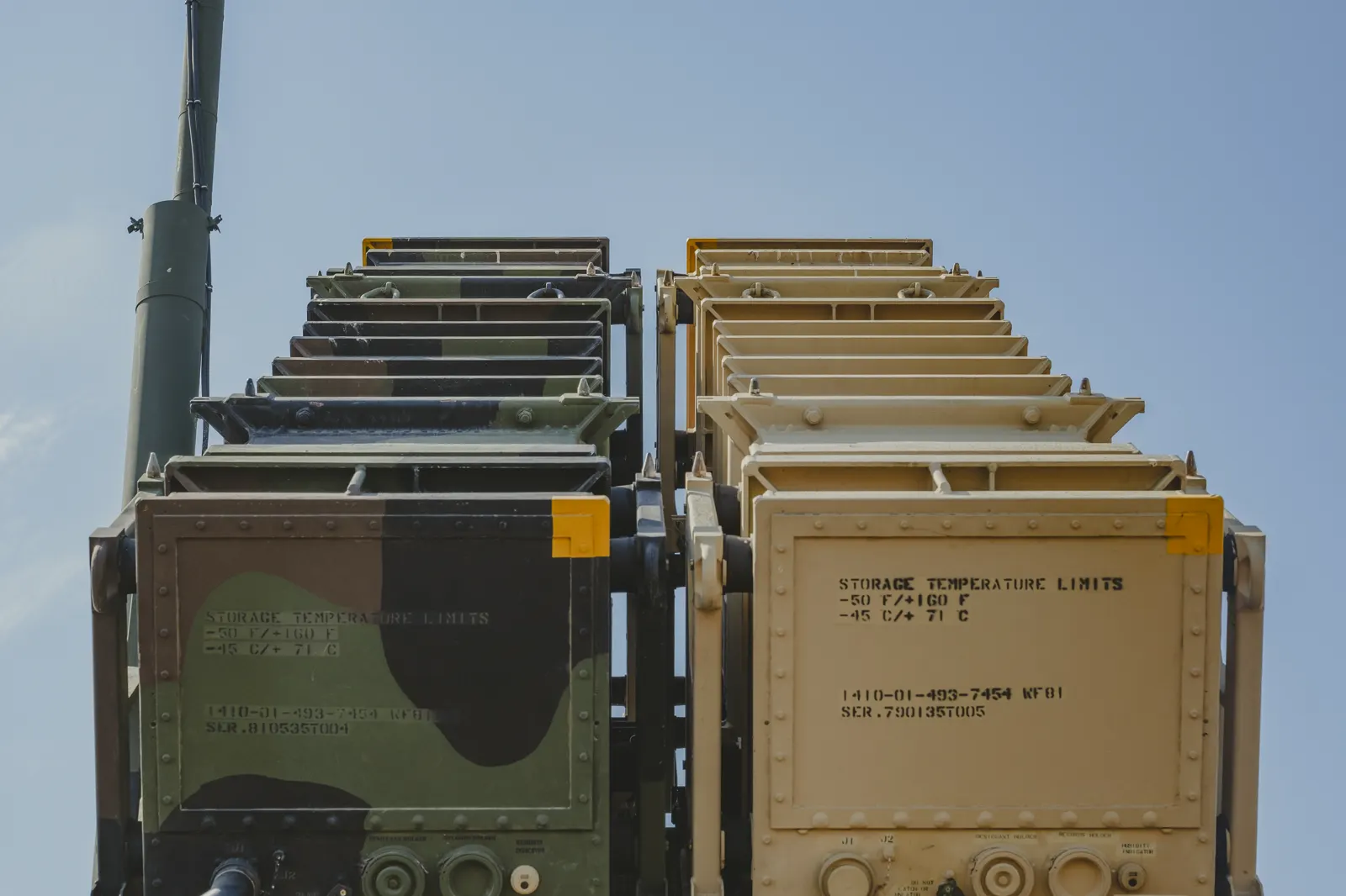 Primer plano de los contenedores de lanzamiento de un sistema antiaéreo Patriot, elevados contra un cielo despejado: cuatro tubos con camuflaje verde a la izquierda y cuatro de color arena a la derecha