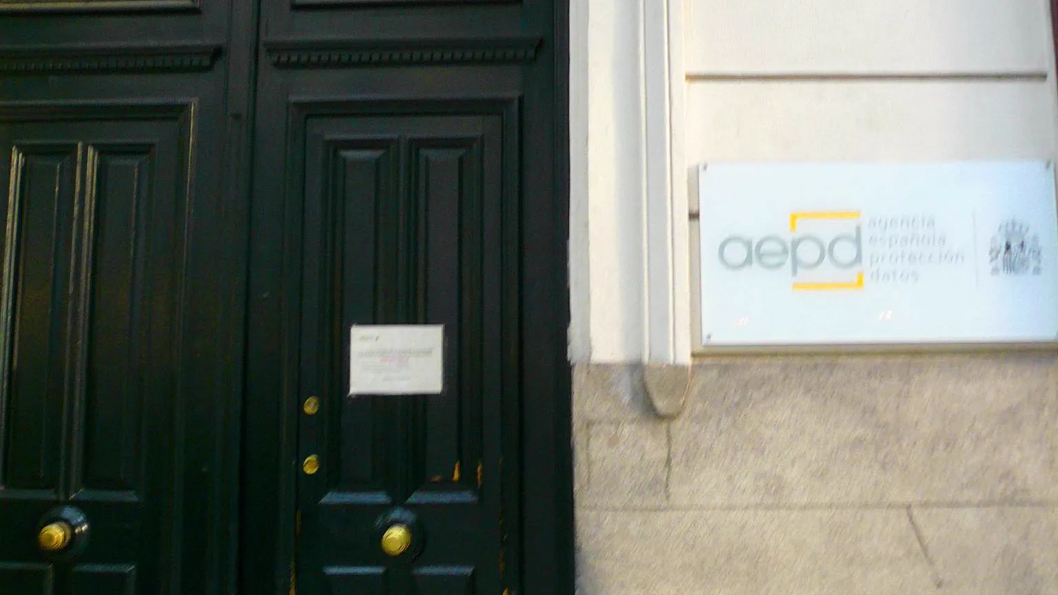 Puerta de madera oscura y placa blanca con el logotipo de la Agencia Española de Protección de Datos en la fachada de su sede de Madrid