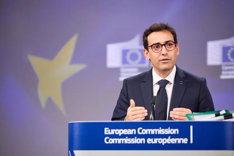 Stéphane Séjourné gesticula tras el atril de la sala de prensa de la Comisión Europea, con el logotipo «European Commission» en el frontal y una estrella amarilla sobre fondo azul detrás.