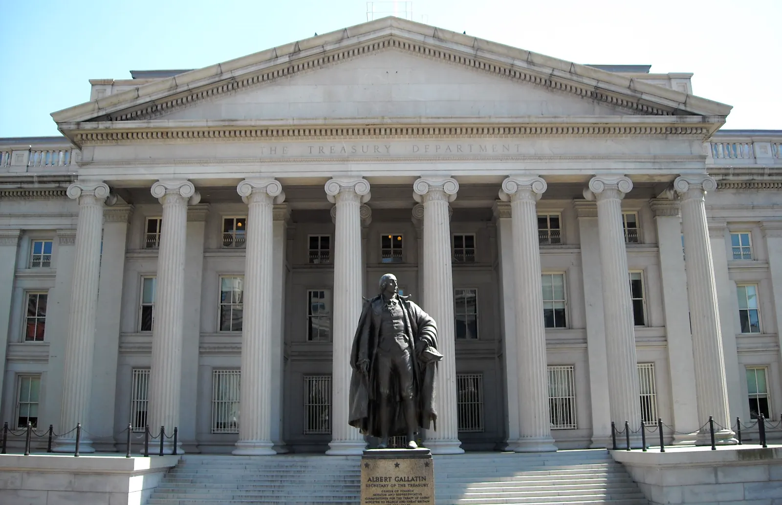 Fachada norte del Departamento del Tesoro de Estados Unidos, con columnas jónicas y la inscripción «The Treasury Department» en el friso; delante, la estatua de bronce de Albert Gallatin sobre su pedestal.