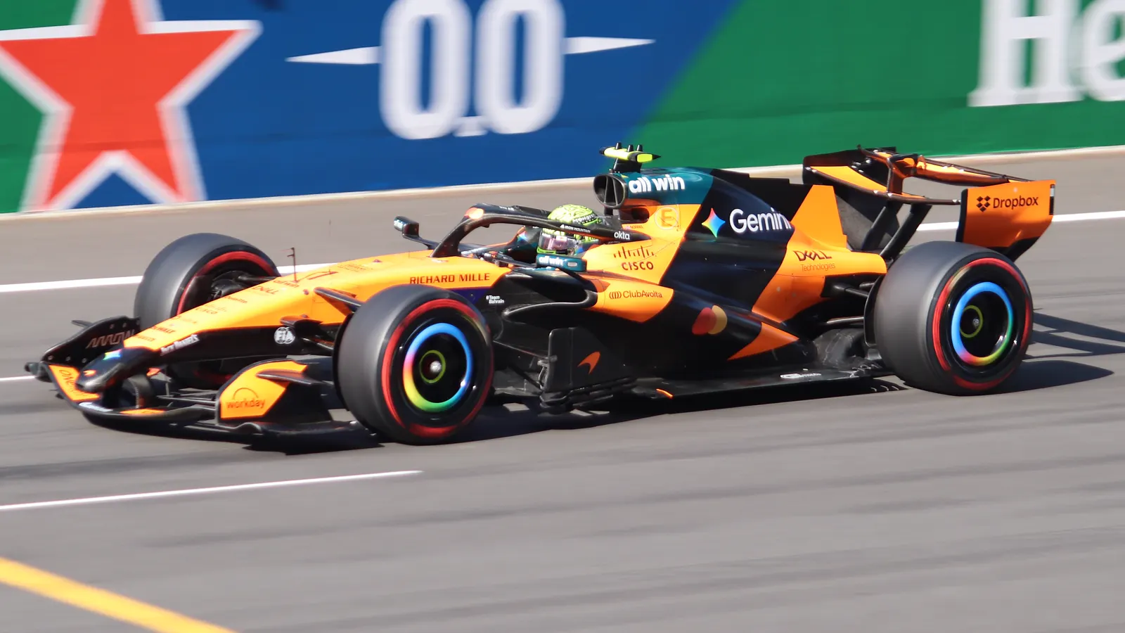Monoplaza de Fórmula 1 de McLaren, naranja y negro, rodando a gran velocidad sobre el asfalto de un circuito