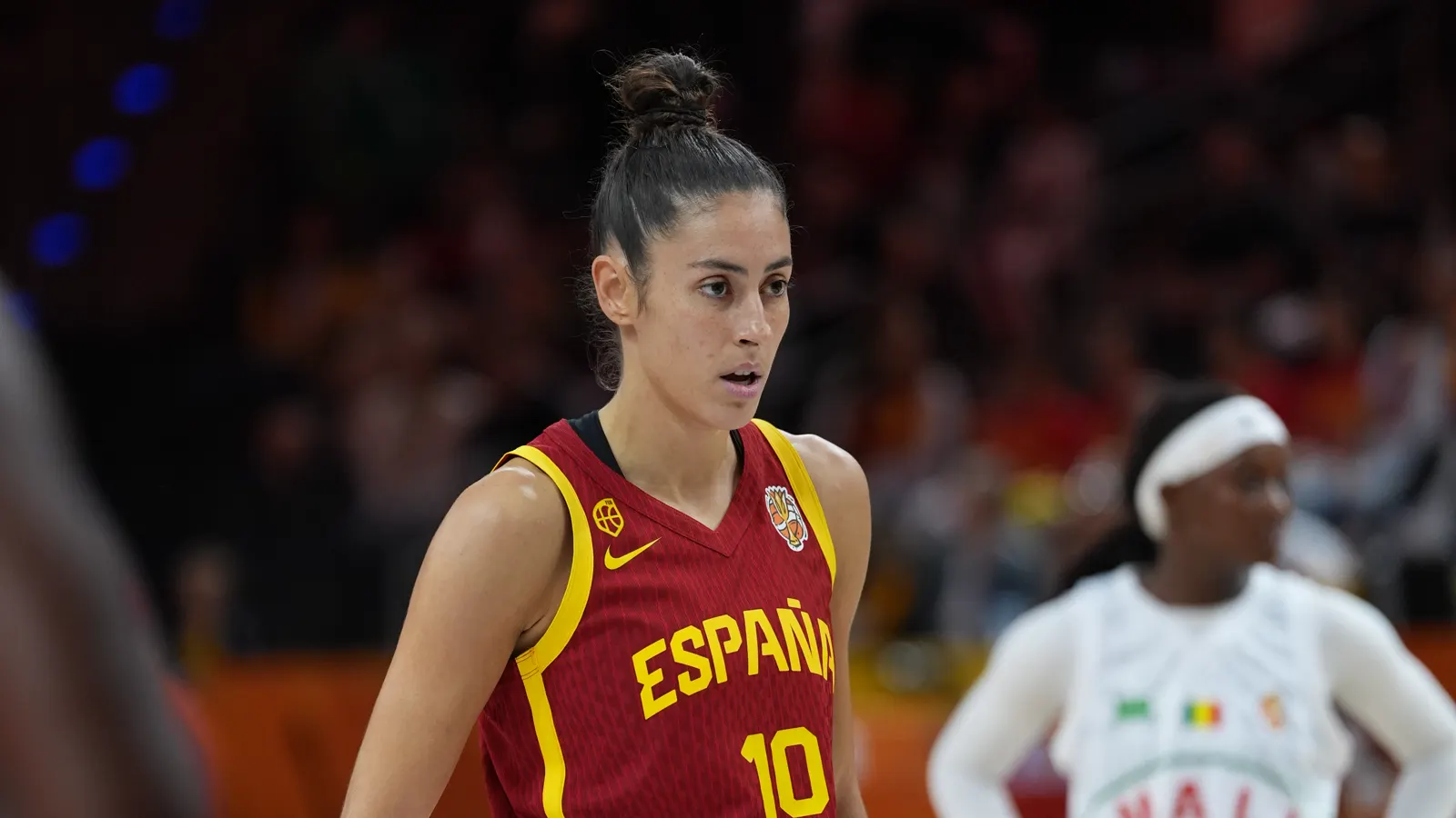 María Conde, con la camiseta roja de España y el dorsal 10, en primer plano sobre la pista; al fondo, desenfocada, una jugadora de Malí de blanco
