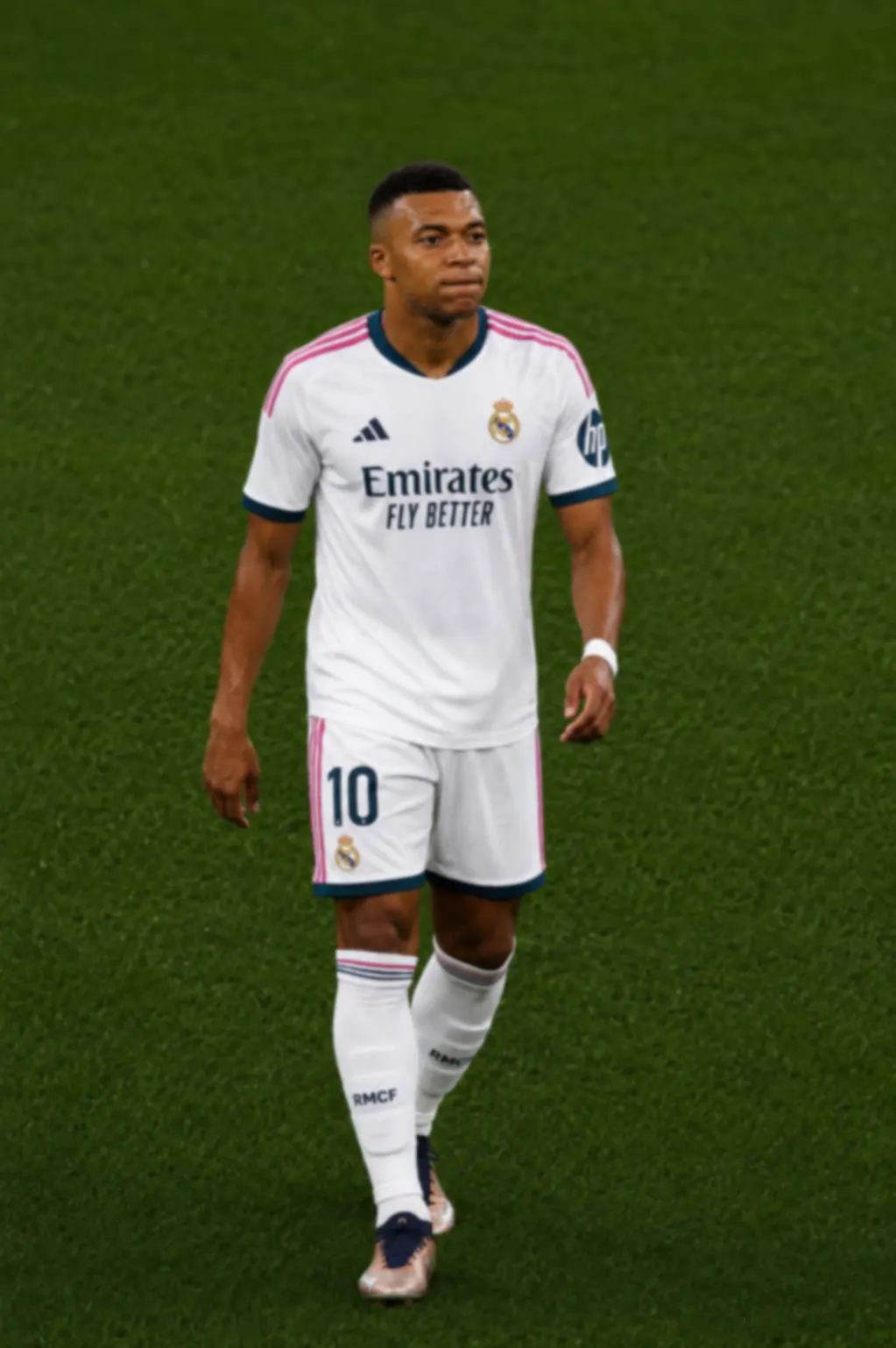 Kylian Mbappé, con la camiseta blanca del Real Madrid y el dorsal 10, camina sobre el césped iluminado del Santiago Bernabéu durante un partido.