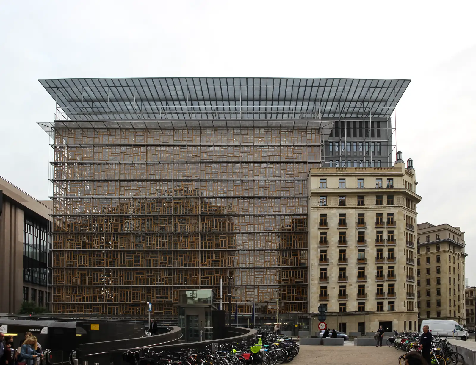 Fachada acristalada del edificio Europa, sede del Consejo de la Unión Europea, en el barrio europeo de Bruselas, con bicicletas aparcadas y viandantes en la explanada de la entrada.